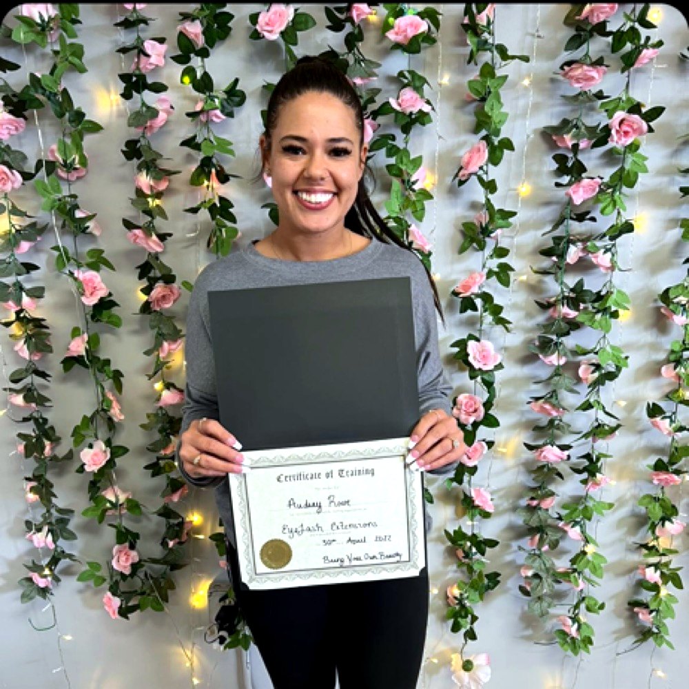 Audrey Fisher, owner of Lashed AF, smiling in front of a flower wall